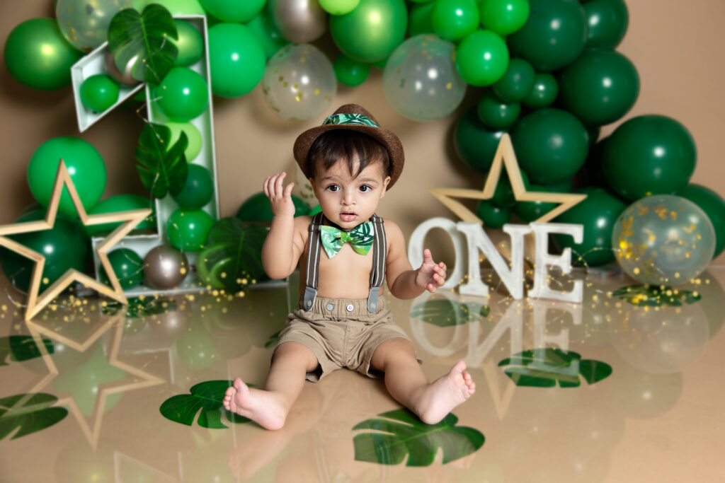 Baby boy birthday photoshoot in decoration with green balloons on beige background with big number one and stars. 